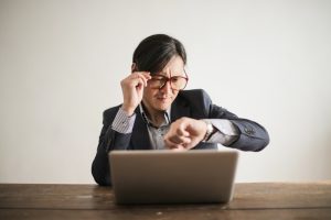 Asian gentleman in a suit looking at his wrist watch while working on a laptop. Image for the ResultsResourcing ROI Calculator free tool.