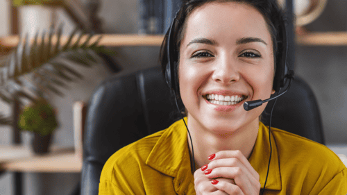 A freelance customer service representative working for a business is wearing a headset and smiling.