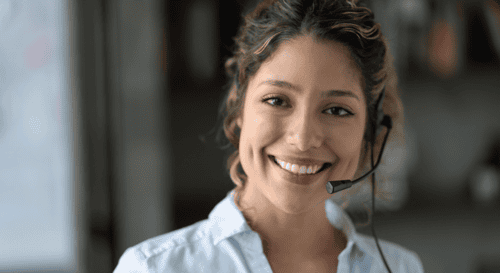 A woman working as a freelance virtual assistant is smiling into the camera.