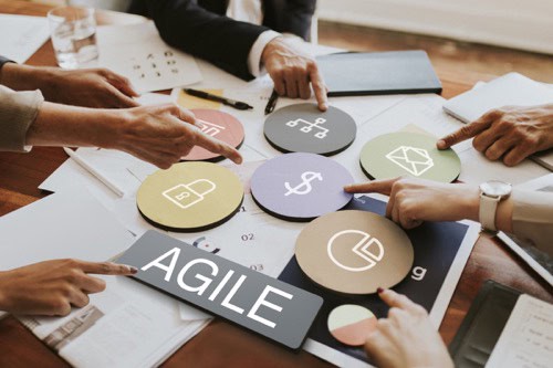 A group of business leaders sits around a table and point at icons symbolizing ways to be more agile. Agile talent strategy